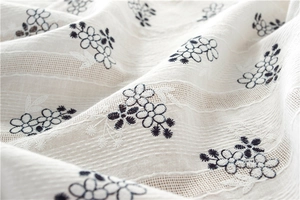 Detail of white cotton tablecloth with blue floral embroidery and openwork lace stripes