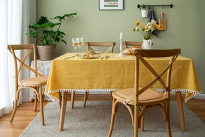 Detail of yellow cotton tablecloth featuring white pom-pom fringe on a wooden table