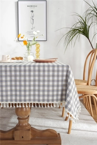 Close-up of gray and yellow plaid tablecloth with white fringe tassels on a wooden table