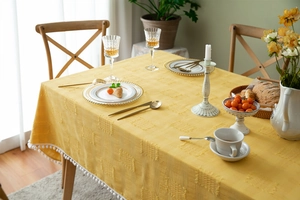 Detail of yellow cotton tablecloth featuring 3D checkered texture and white pom-pom fringe