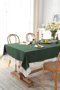Detail of dark green cotton tablecloth featuring wide white lace edges on a wooden table