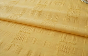 Close-up of yellow textured fabric with square jacquard patterns and soft tassel edges