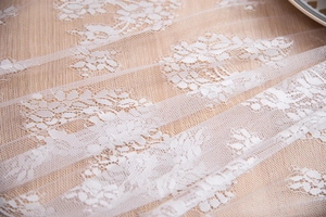 Close-up of intricate white floral lace mesh fabric with detailed rose embroidery patterns