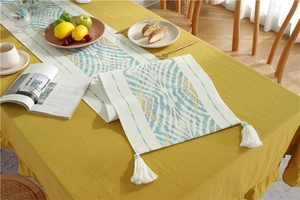 Detail of teal and gold geometric patterned table runner with white fringe tassels