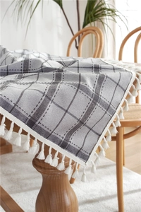 Detail of grey and white plaid tablecloth with dense white fringe on a wooden table