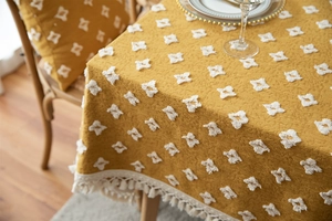 Detail of yellow rectangular tablecloth with white tufted geometric patterns and tassels
