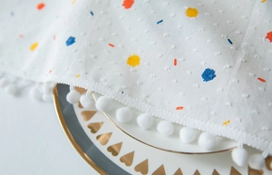 Detail of white cotton tablecloth with colorful dots and fluffy pom-pom fringe trim