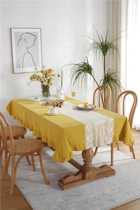 Detail of ginger yellow cotton tablecloth with elegant ruffles and white lace table runner