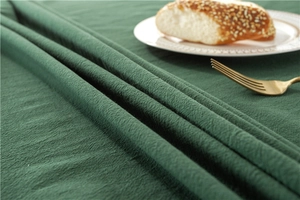 Detail of dark green cotton tablecloth featuring rustic texture and fringe lace border