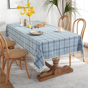 Blue plaid tablecloth with white fringe tassels on a wooden dining table in Nordic style