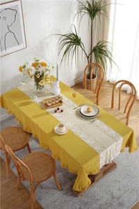 Detail of yellow cotton tablecloth with white floral lace runner and ruffled edges