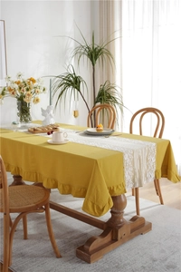 Detail of yellow cotton tablecloth with ruffled edges and white floral lace table runner