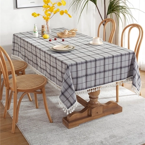 Grey plaid tablecloth with white fringe tassels on a wooden dining table in a cozy room