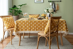 Close-up of bohemian yellow tablecloth featuring white tufted patterns and fringe edges