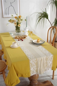 Detail of mustard yellow cotton tablecloth with lace table runner and ruffle edges