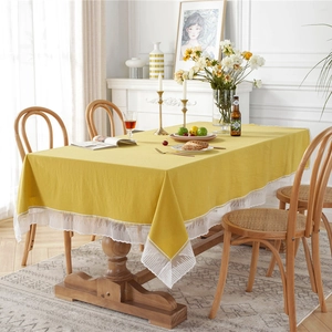 Solid ginger yellow cotton tablecloth with white lace edges and fringe on a wooden dining table