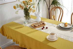 Detail of warm yellow cotton tablecloth featuring elegant ruffled edges and white lace runner