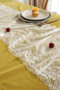 Detailed close-up of white lace table runner with floral embroidery on yellow tablecloth
