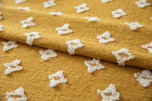 Macro detail of mustard yellow textured fabric with white tufted diamond patterns