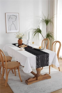 Detail of white ruffled cotton tablecloth with elegant black floral lace table runner