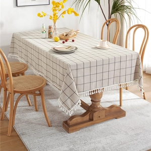 Minimalist beige checkered tablecloth with white tassels on a rectangular wooden table