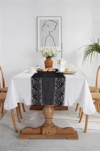 Detail of black floral lace table runner with scalloped edges on white tablecloth
