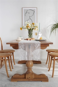 Detail of white lace table runner with floral embroidery on wooden dining table surface