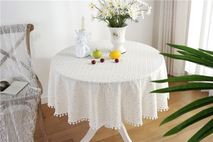 Detail of round yellow polka dot tablecloth with white pom-pom fringe and cotton texture