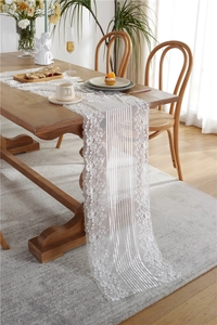 Close-up of white floral lace table runner with intricate embroidery on a wooden table