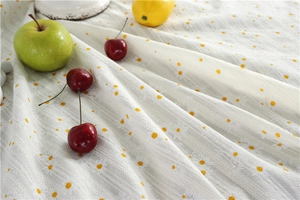 Close-up of white cotton tablecloth with yellow daisy embroidery and lace cutouts