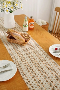 Detailed close-up of cream crochet table runner with hollow geometric patterns and boho tassels