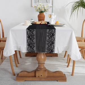 Modern black lace table runner with floral embroidery over white ruffled tablecloth