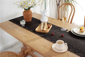 Close-up of black floral lace table runner with stripes on a wooden dining table