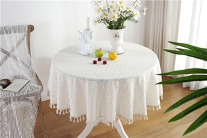 Detail of round cotton tablecloth with yellow polka dots and tassel trim in cozy home setting