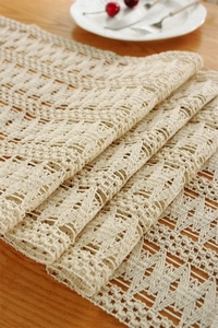 Detail of beige hollow crochet table runner showing intricate wavy woven patterns on wood