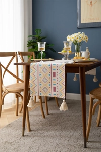 Close-up of bohemian geometric table runner with cotton tassels on a dark wood table