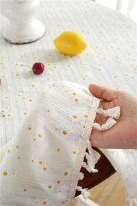 Close-up of cotton floral tablecloth fabric featuring yellow daisy print and beige tassels
