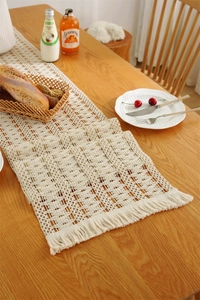 Detail of woven table runner with geometric lace patterns and decorative fringe tassels