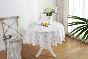 Detail of floral round cotton tablecloth featuring delicate pom-pom fringe edges