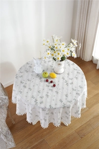 Detail of white cotton round tablecloth with green floral pattern and pom-pom trim