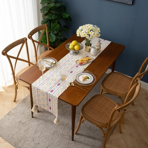 Detail of colorful geometric table runner with cream tassels on a rustic wood dining table