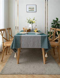 Detail of dark green geometric plaid tablecloth with white fringe trim on a wooden table