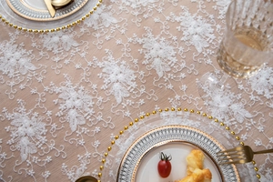 Détail de nappe en dentelle blanche brodée avec vaisselle dorée élégante et verres
