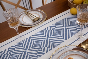 Detail of blue geometric print table runner with cotton tassels on a wooden table
