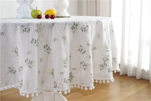 Detail of floral round tablecloth with white pom-pom trim and elegant hanging texture