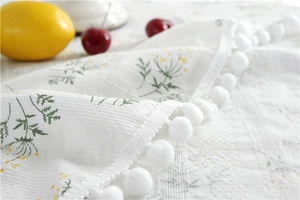 Close-up of floral cotton tablecloth fabric with white pom-pom fringe details