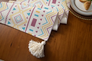 Detailed close-up of woven table runner with colorful geometric patterns and cotton tassels