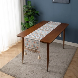 Ethnic geometric table runner with colorful patterns and cotton tassels on a wooden table