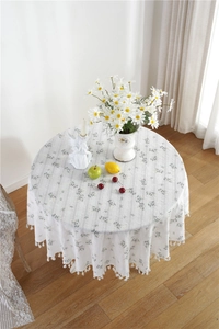 Detailed close-up of white round floral cotton tablecloth with elegant fringe tassels