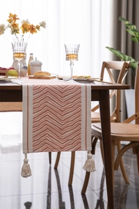 Detail of colorful geometric wave pattern table runner with cotton tassels on wood table